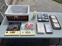 Full view of all items on table: wicker basket, two vintage cassette storytelling sets, two VHS tapes, wooden framed barometer, battery operated candle, and clock.
