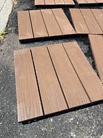 Close-up of the top surface of one brown composite decking tile showing four horizontal planks on a black plastic interlocking base.