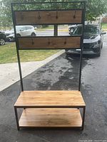 Front view of the entrance bench showing metal frame, wooden seat, lower shelf, and two wood panels with hooks.