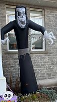 Front view of the black inflatable grim reaper with large skull face and skeletal hands, displayed outdoors.