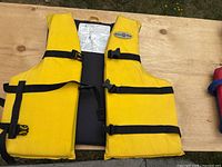 Photo showing two yellow Buoy-O-Boy personal flotation devices laid flat with black straps and buckles