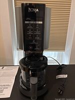 Ninja Creami ice cream maker machine plugged in and assembled, shown with container inserted and control panel visible.