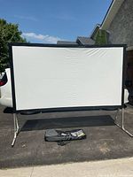 Full view of the 120-inch outdoor projection screen assembled, showing white screen material with black border and aluminum frame, placed outside on pavement.