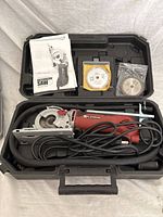 Electric mini saw with power cord inside black molded carrying case along with instruction manual and three saw blades.