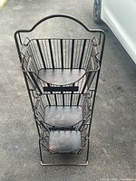 Front view of the three-tier metal basket stand showing wire baskets with wooden bases and a handle on top.