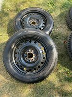 Four black steel rims each mounted with a Firestone Winterforce 2 winter tire, laid on grass outdoors.