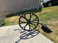 Side view of snow shovel showing large spoked wheel acting as a lever and wide plastic scoop blade on grass.