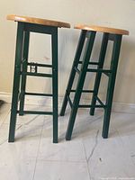 Two of the three stools side view showing green legs and wood seats