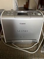 Front view of Canon Selphy printer showing logo, paper tray slot and power cord