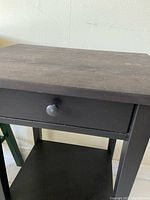 Front view of black wood side table showing drawer and shelf