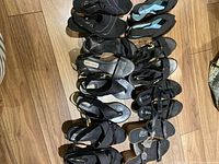 Group of eight pairs of black sandals arranged on wooden floor