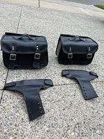 Two black leather saddlebags and two leather mounting yokes on pavement