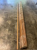 Full view of narrow cedar trim pieces and wider boards wrapped in plastic on concrete floor.