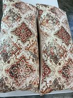 Two rectangular couch pillows with detailed geometric patterns in cream, orange, grey, and red colors