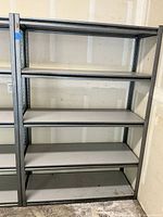 Full view of steel metal shelving unit with four laminate wood shelves, showing overall condition with bottom shelf discoloration.