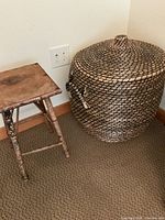 Side view of large woven basket with lid next to a small wooden stool.