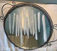 Photo of a round mirrored tray with white hanging crystals placed in parallel lines across the mirror surface, with ornate black rim and handles visible.