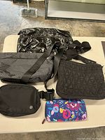 Five small travel handbags and a pouch laid out on a table, showing variety in style and material.