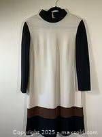 Front view of vintage 1960's knit dress featuring cream body with black long sleeves, and brown and black color block hem.