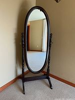Front view of a freestanding oval mirror with dark wooden frame and turned supports.