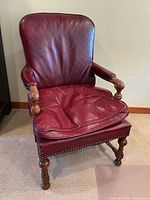 Front view of vintage red leather armchair with wooden frame and brass button trim.