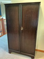 Exterior front view of closed wardrobe showing two paneled doors, brass key lock and dark wood finish.