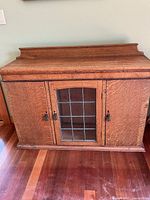 Front view of vintage sideboard showing wood finish, two side doors, and central leaded glass door