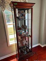 Front view of tall wood veneer and glass display cabinet showing three glass shelves and mirrored back