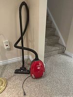 Vacuum with hose and floor head standing against stair wall
