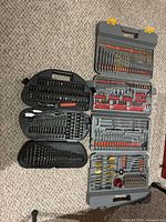 Overview of three open drill and driver bit sets in grey and black cases