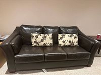 Front view of dark brown leather sofa with two floral cushions