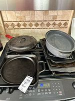 Stacked cast iron pieces, enamel roaster, cookie sheets on stove