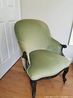 Full view of sage green upholstered armchair against wall