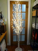 Full view of illuminated birch LED tree standing in front of door