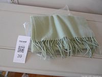 Folded light mint green cashmere scarf in plastic sleeve with fringe visible