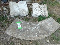 Two ornate cement pedestal legs and curved seat section laid on grass