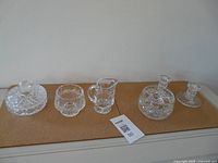 Five crystal items on surface: covered bowl, open bowl, creamer, two candle holders
