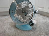 Front angled view of turquoise metal table fan showing blades and grille
