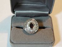 ring facing forward in open grey box showing garnet-tone stone and crystal halo
