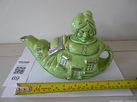Left side view of teapot showing old woman figure, shoe windows and measuring tape