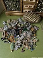 Overview of brass clutch and pile of costume jewelry on green surface