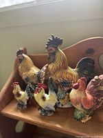 Front view of five ceramic rooster, hen and chick figurines on wooden shelf