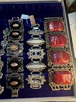 Tray showing three of the vintage bracelets: black enamel with oval art glass, filigree with opalescent stones and red marbled cabochon bracelet