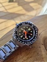 Front angle view of watch on wooden surface showing bezel, dial and bracelet