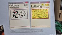 Front and back cover of two calligraphy instruction books titled 'Calligraphy & Lettering' and 'Lettering' placed side by side with a ruler nearby for scale.