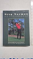 Front cover of Greg Norman Advanced Golf book showing Greg Norman mid-swing in red shirt with trees in background.