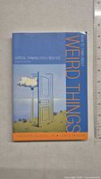 Front cover of the paperback book titled 'How to Think About Weird Things: Critical Thinking for a New Age, Fourth Edition' by Theodore Schick Jr. and Lewis Vaughn on a plain surface with ruler for scale.
