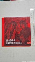 Front cover of the Legends: Untold Stories book showing red monochrome image of two musicians with the title and Ray-Ban branding.