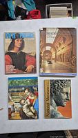 Top view of 4 art books featuring classical artwork and museum interiors on covers.
