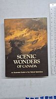 Front cover of 'Scenic Wonders of Canada' illustrated guide book showing a mountain scene with dramatic clouds and sunlight.